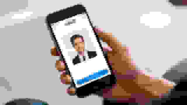 A hand holds a smartphone displaying the LinkedIn app, showing a professional man's photo being cropped for a profile picture.