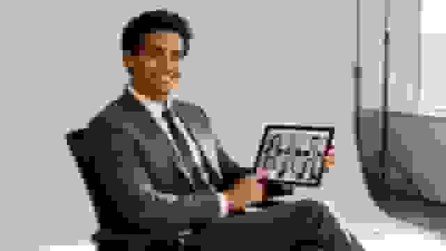 Smiling businessman in a suit holds a tablet displaying a grid of diverse professional headshots.